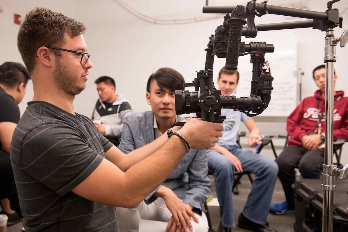 A small room of Emerson College film students being shown how to use a piece of camera equipment
