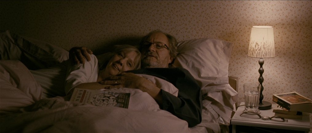 Film still from Another Year (2010) showing older couple cuddling in bed