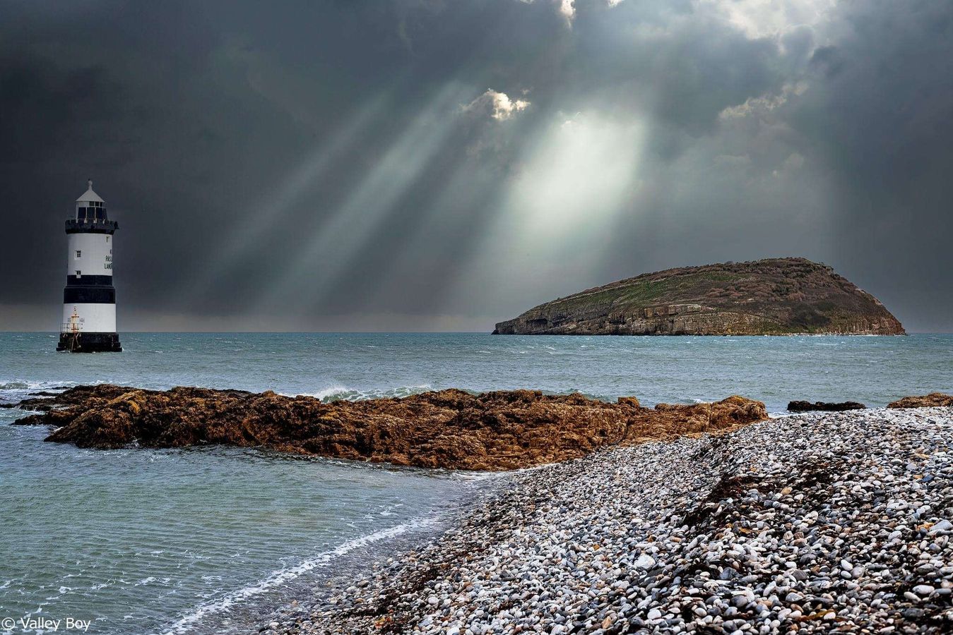 Trwyn Du Lighthouse on Anglesey with dramatic storm light rays breaking through dark clouds over the sea