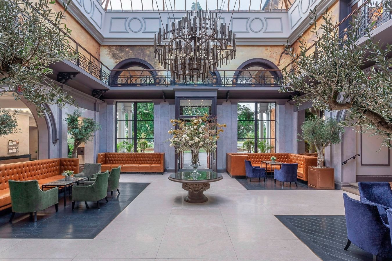 Grand hotel lobby atrium with glass skylight, chandelier, olive trees and Chesterfield sofas in Surrey