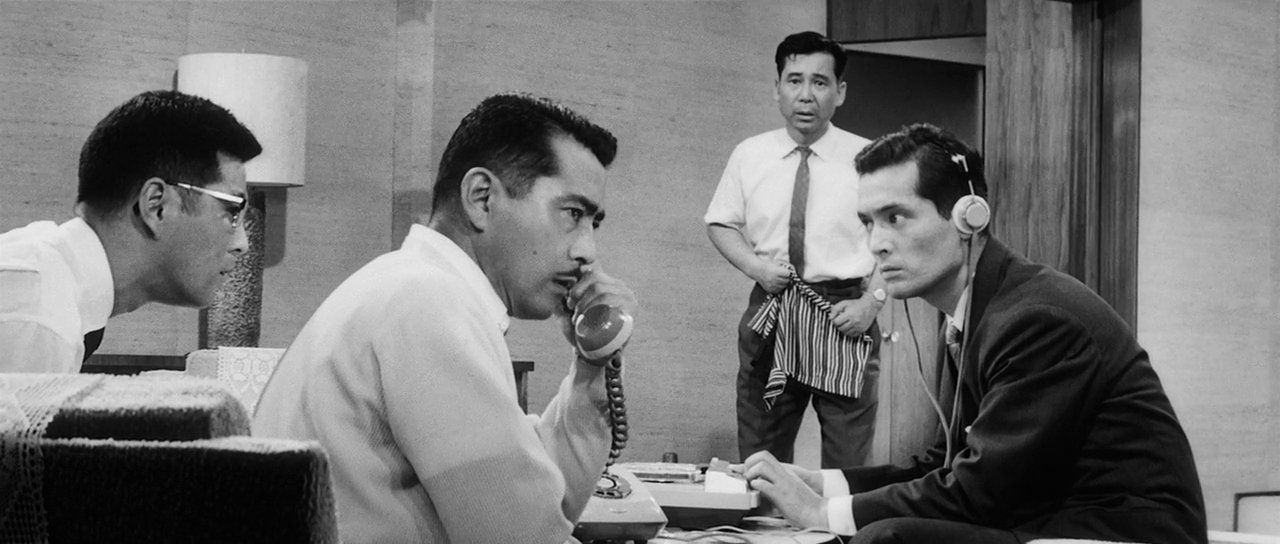 film still from High and Low showing four men sat around listening to a phone call