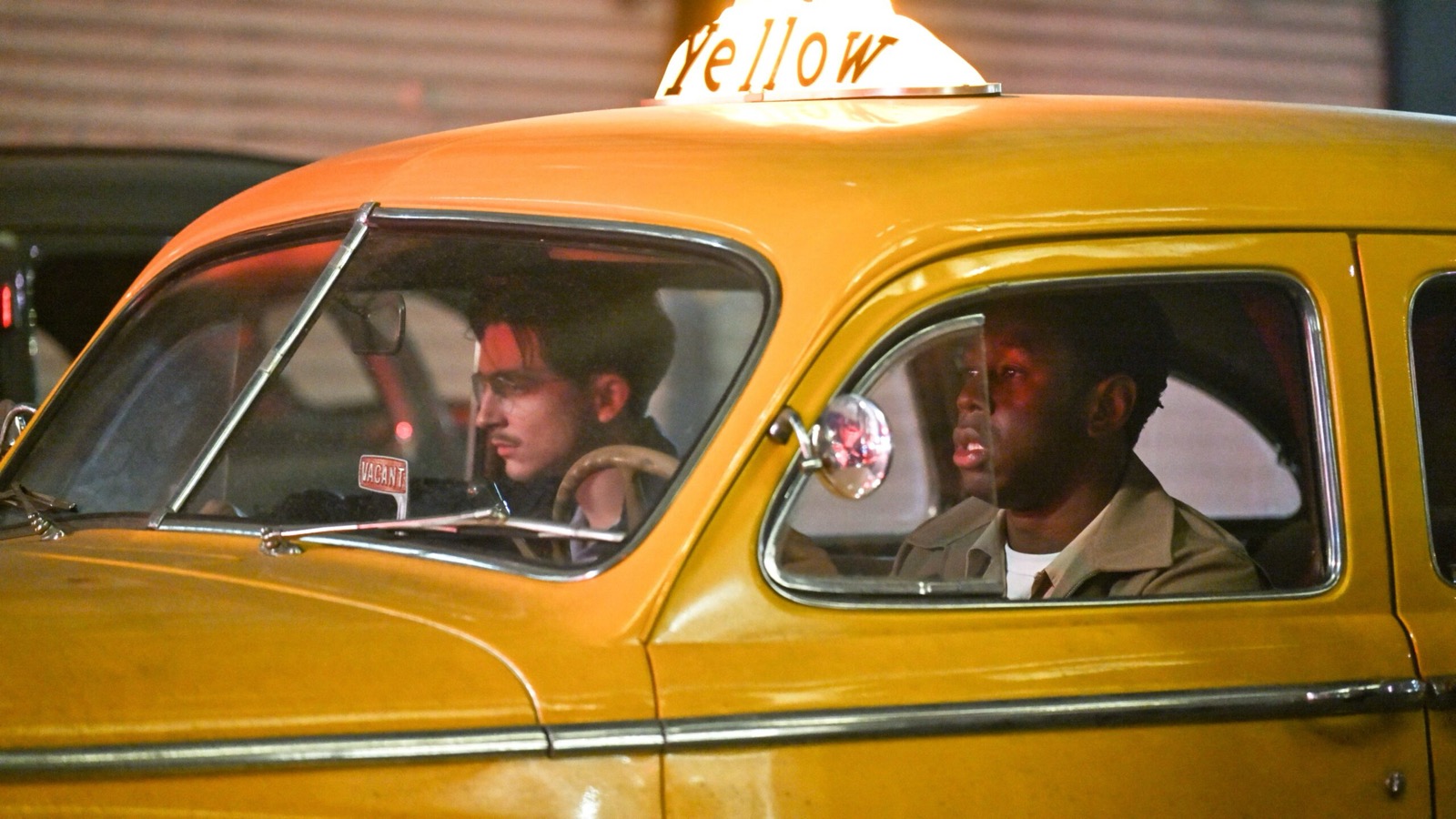 film still showing two characters in a yellow taxi car