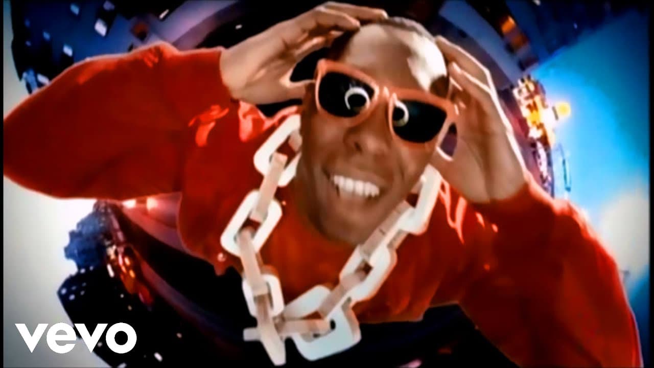Dizzee Rascal Bonkers music video still with performer in red top, oversized sunglasses and chain necklace in a colourful surreal setting
