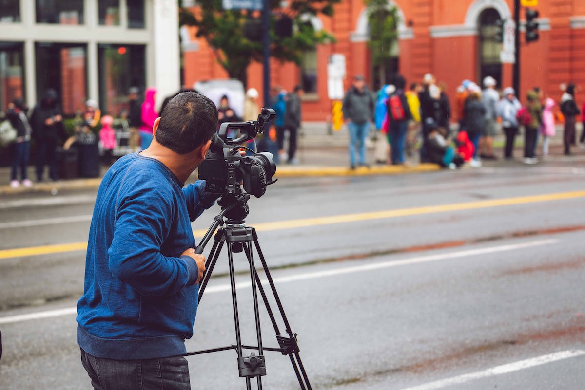 Videographer with professional camera on tripod filming on a busy London street, requiring a London filming permit