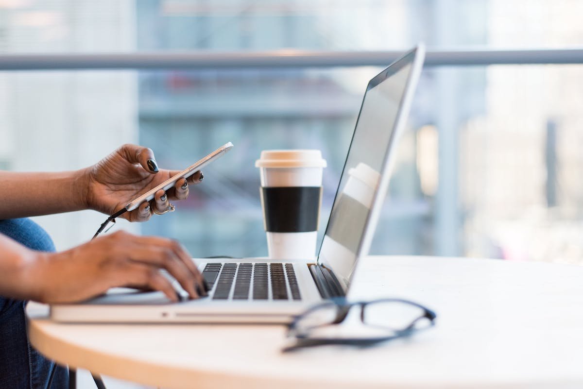 woman with phone in hand working at a desk on a laptop