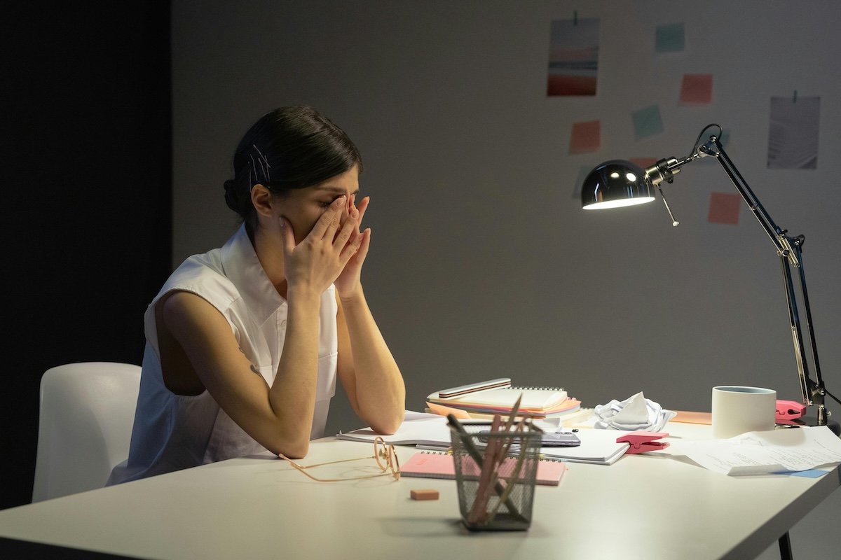 stressed businesswoman sitting at her work desk with hands covering her face