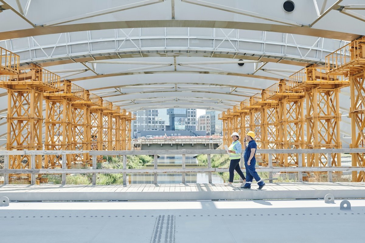 two people walking across a bridge development wearing hard hats and high vis