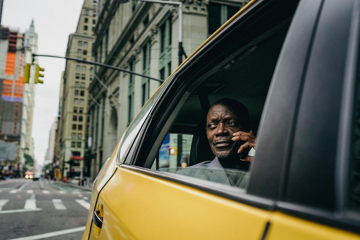 man sitting by the window of a yellow taxi driving through New York City