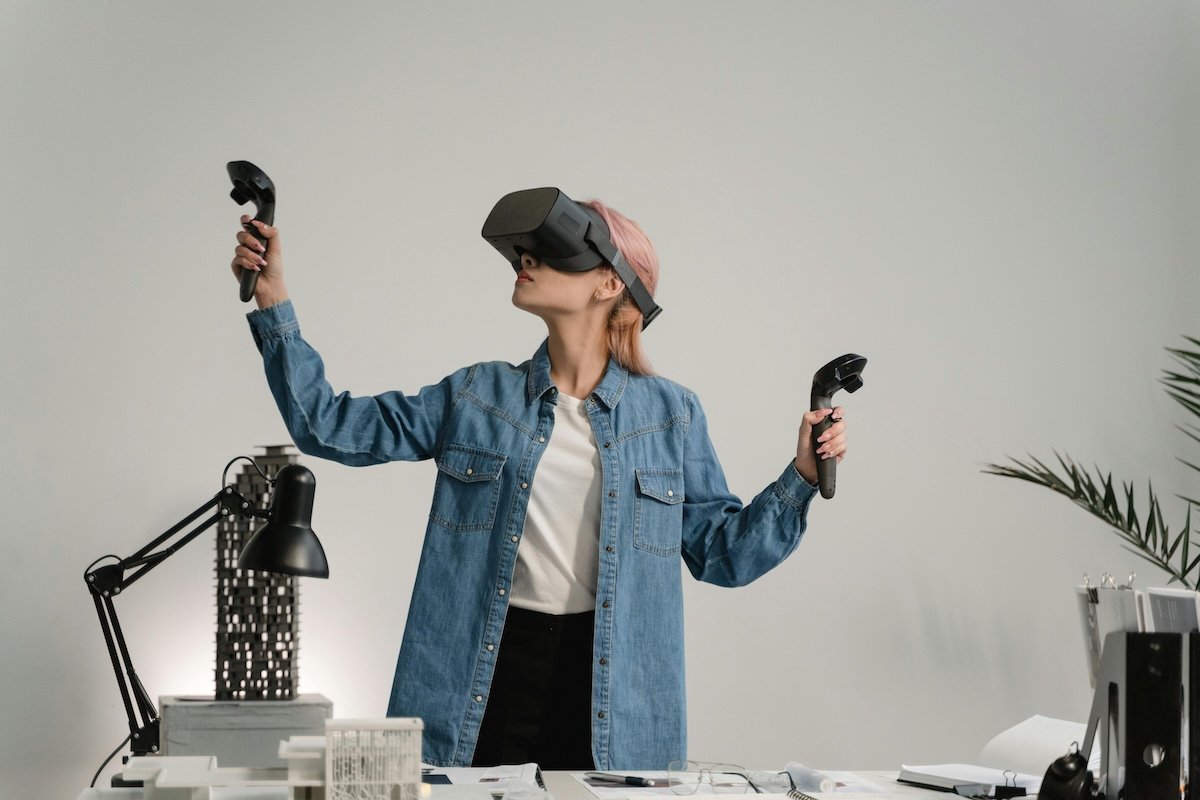 woman standing behind work desk wearing VR headset with controllers in her hands