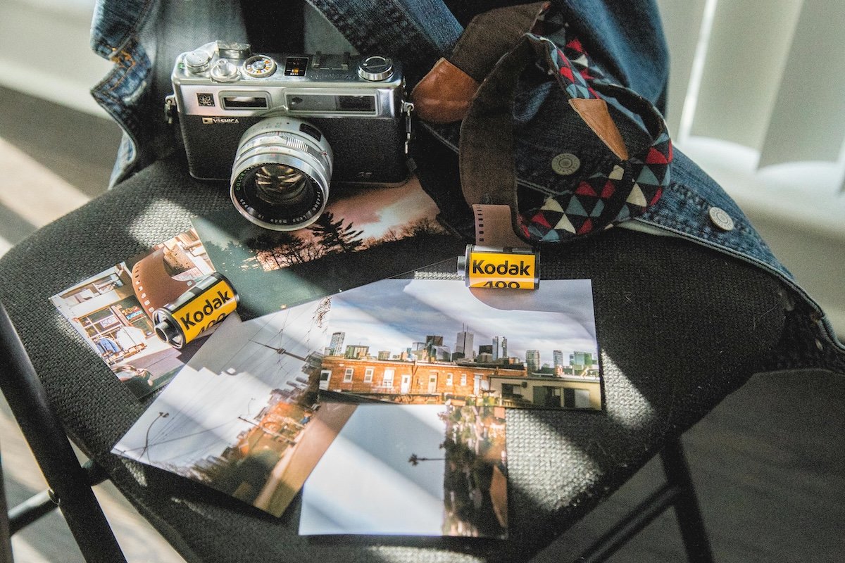 Rolls of Kodak film, printed photos and a classic film camera laid out on a chair